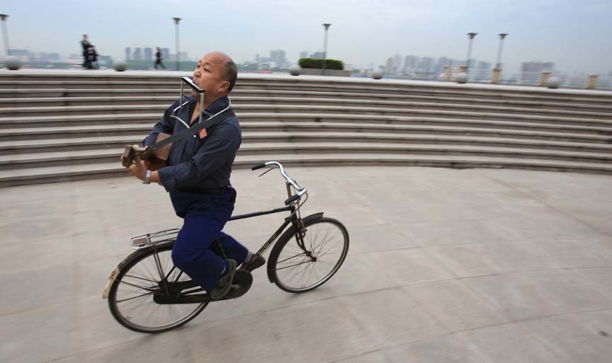 自行车上的音乐人生  他倒骑自行车吹奏口琴、弹吉他……